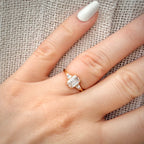 1,20 ct Emerald Cut trilogy-timanttisormus sormessa pellava taustalla