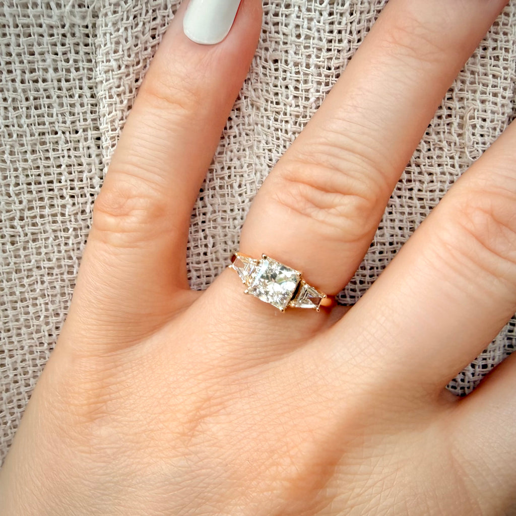 1,69 ct Princess Cut trilogy-timanttisormus sormessa pellava taustalla