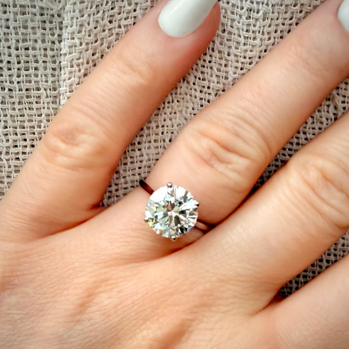 4,01 ct solitaire-timanttisormus sormessa pellava taustalla